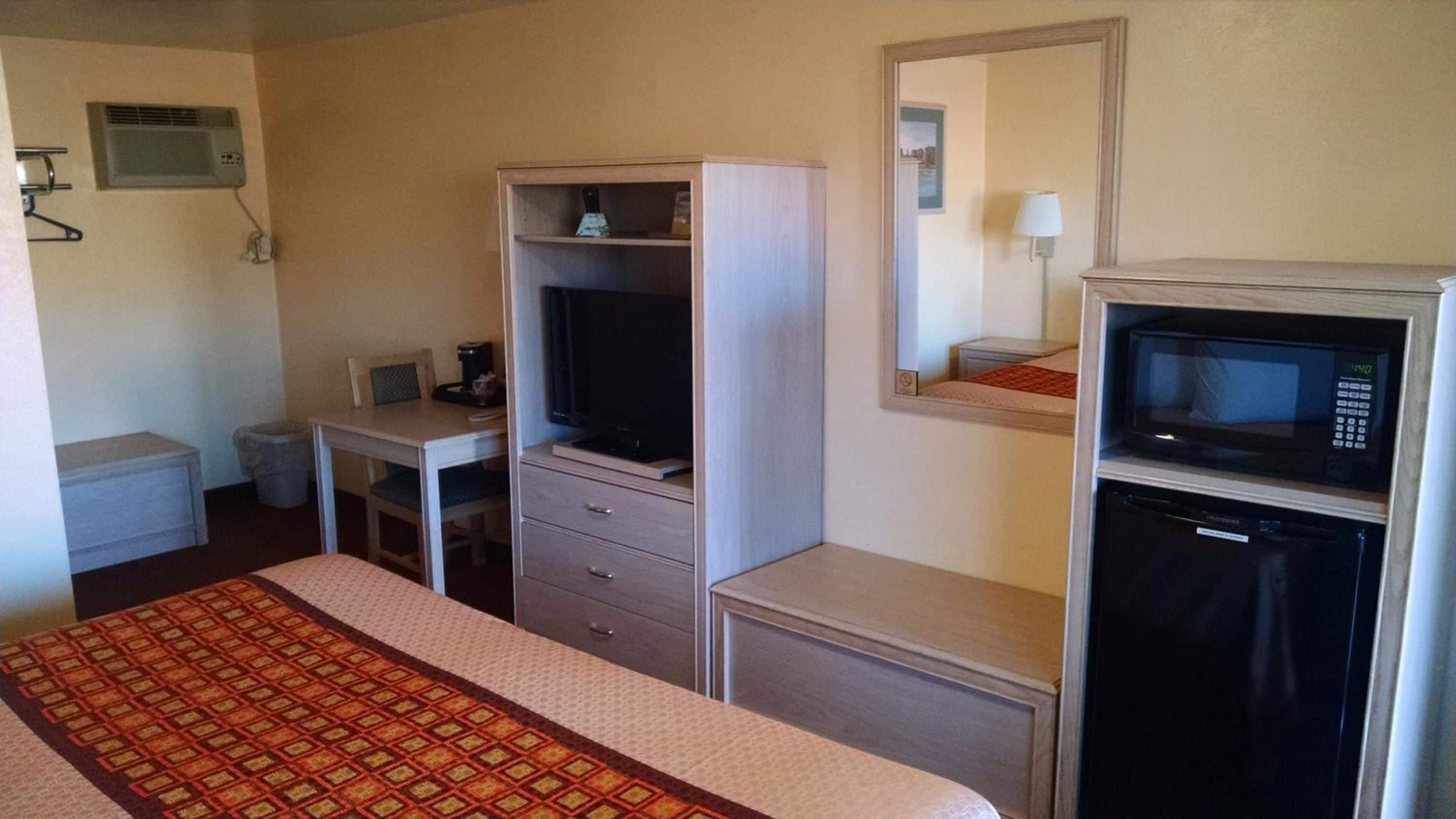 Habitación de hotel con una cama, un escritorio con computadora, televisor, microondas y un mueble pequeño.