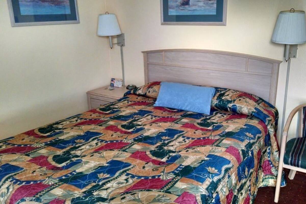 A bed with a colorful quilt, a bedside table with a lamp, and a striped chair.