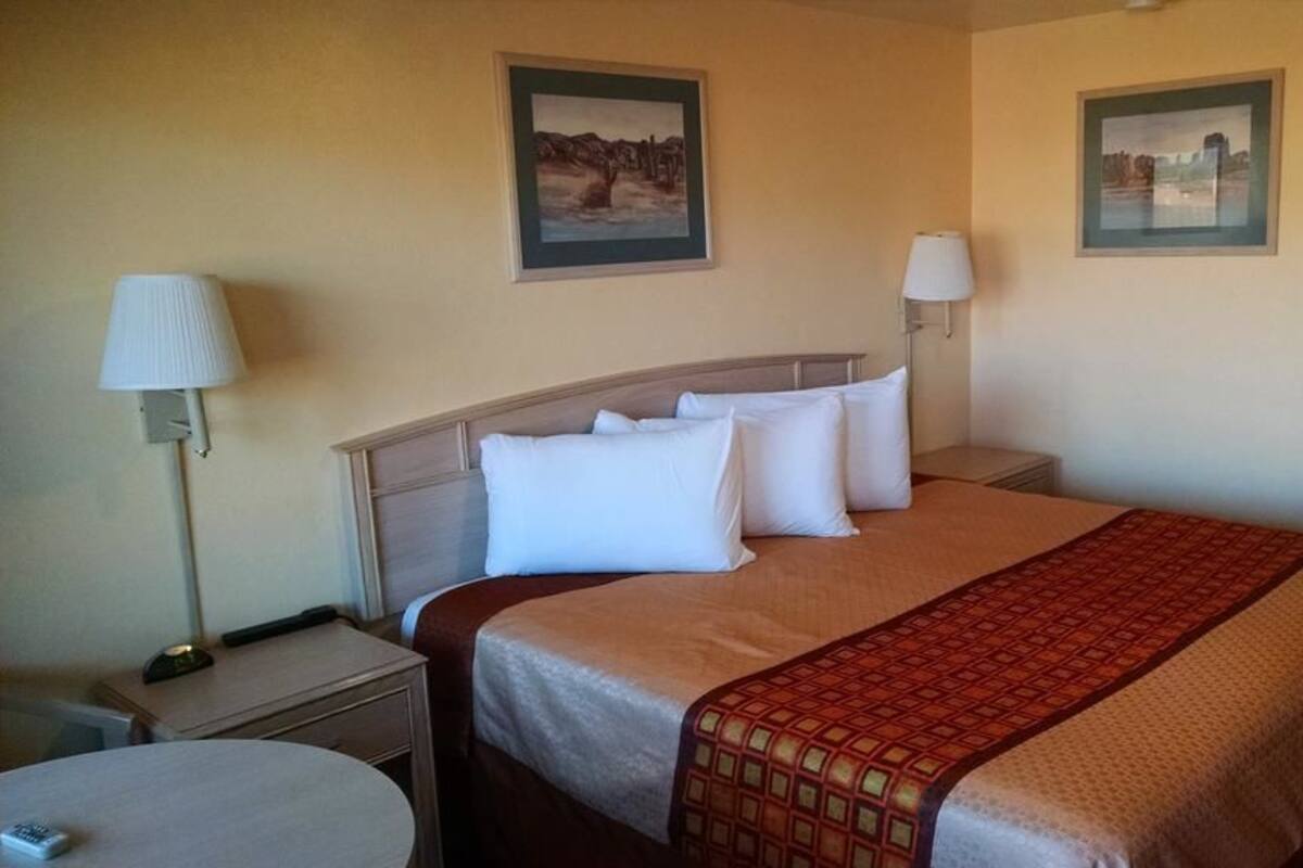 A hotel room with a bed, two bedside lamps, a nightstand, a round table, and two framed pictures on the wall.