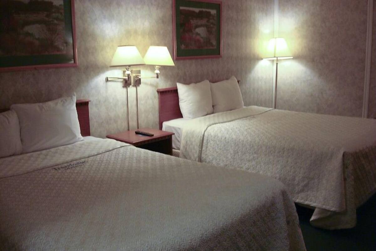 A hotel room with two single beds, a nightstand, and two wall-mounted lamps.