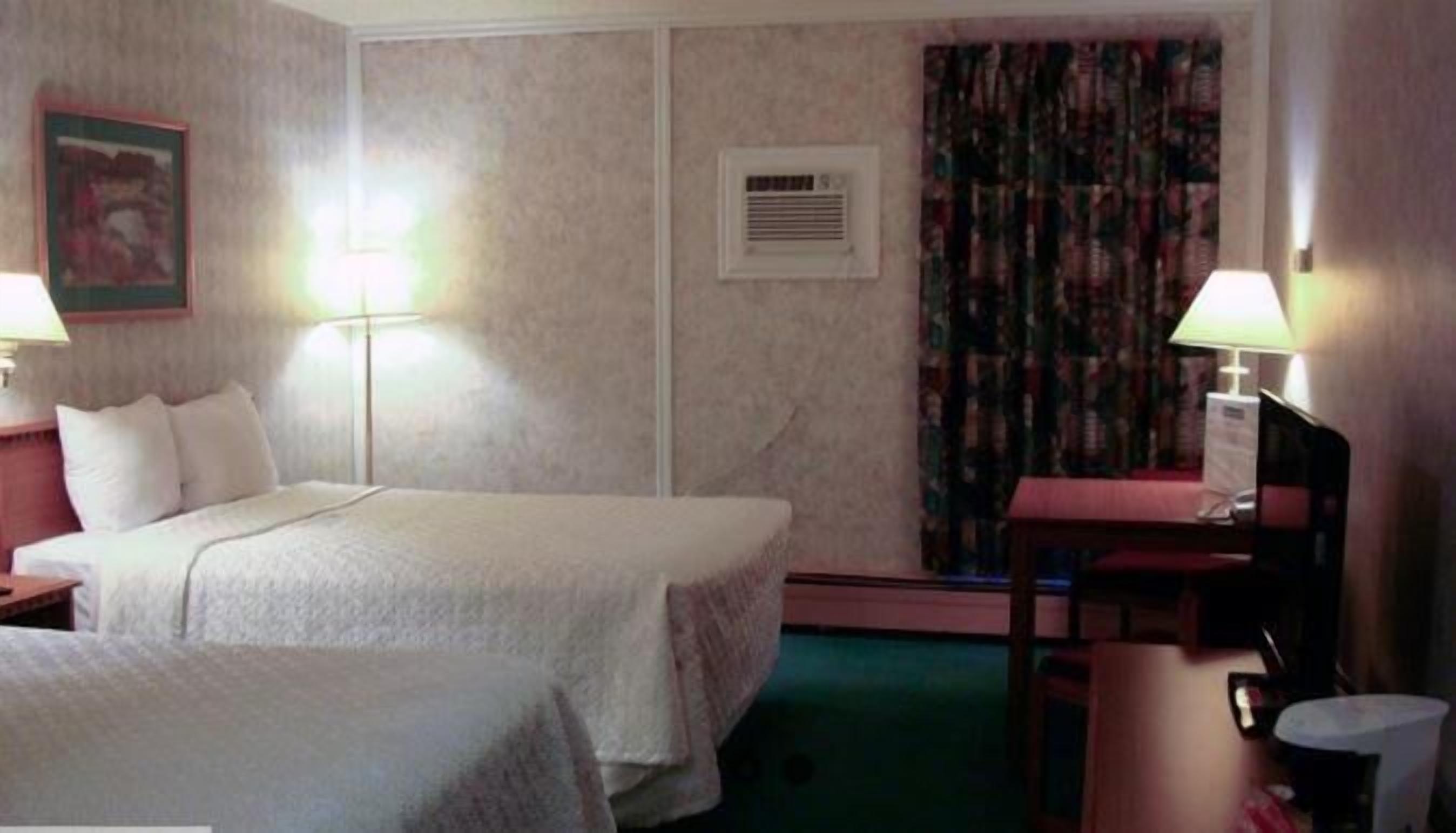 A hotel room with a bed, two bedside tables, a desk with a chair, a lamp, and a window with curtains.