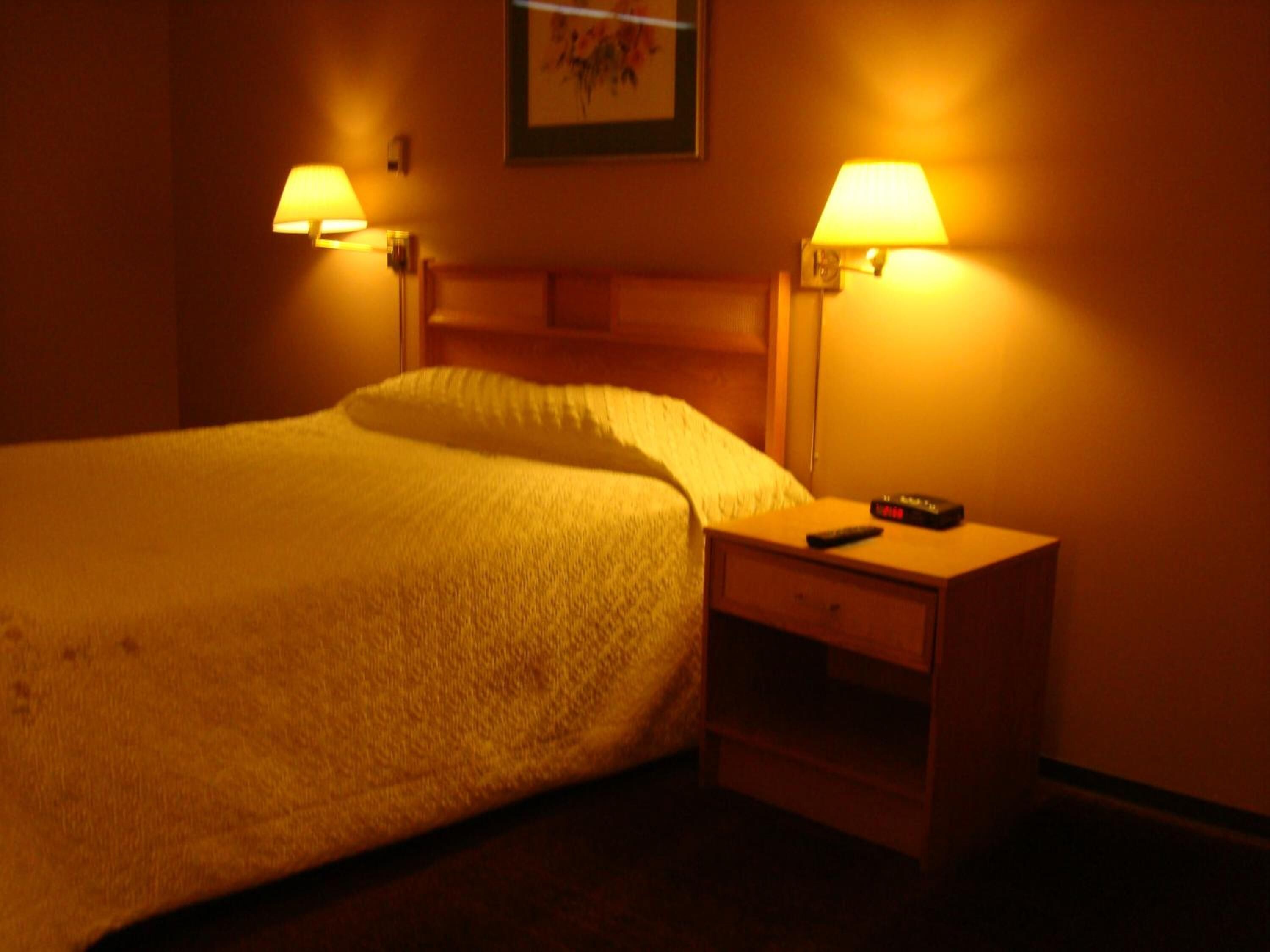 A hotel room with a bed, two bedside lamps, a nightstand, and a remote control.