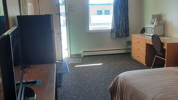 Una habitación de hotel con cama, escritorio con computadora, microondas y ventana con cortinas.