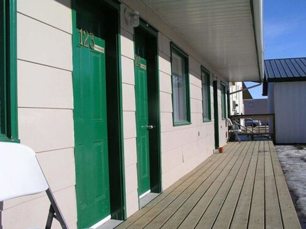 Un bâtiment avec des portes vertes portant les numéros 123 et 124, une terrasse en bois et un espace couvert avec un toit en métal.