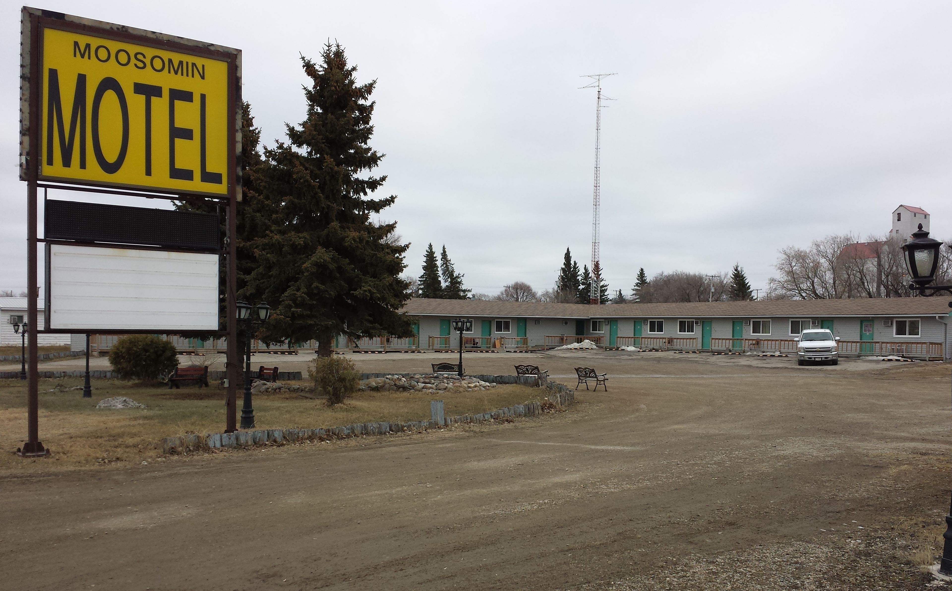 A motel with a signboard, a parking area, and a building with multiple rooms.
