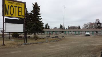 A motel with a signboard, a parking area, and a building with multiple rooms.