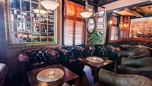 Un área de bar acogedora con asientos de cuero, mesas de madera y lámparas colgantes.