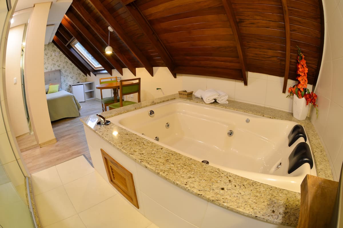 A modern bathroom with a large bathtub, wooden ceiling beams, and a small seating area with a chair and table.
