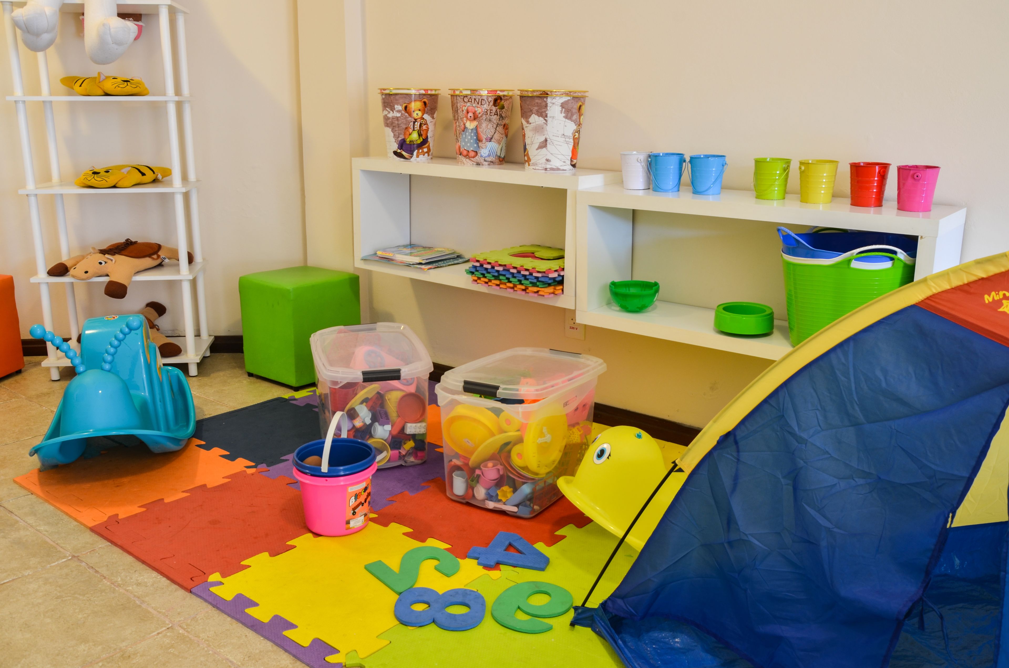 A playroom with a tent, colorful mats, storage bins, and shelves with toys and containers.
