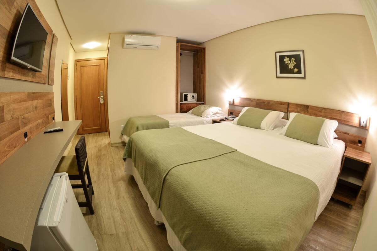 A hotel room with two beds, a desk, a chair, a TV, and a picture on the wall.