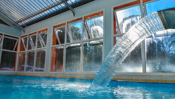 An indoor swimming pool with a water slide, large windows, and a metal roof. - Hotel Renascença (Gramado)