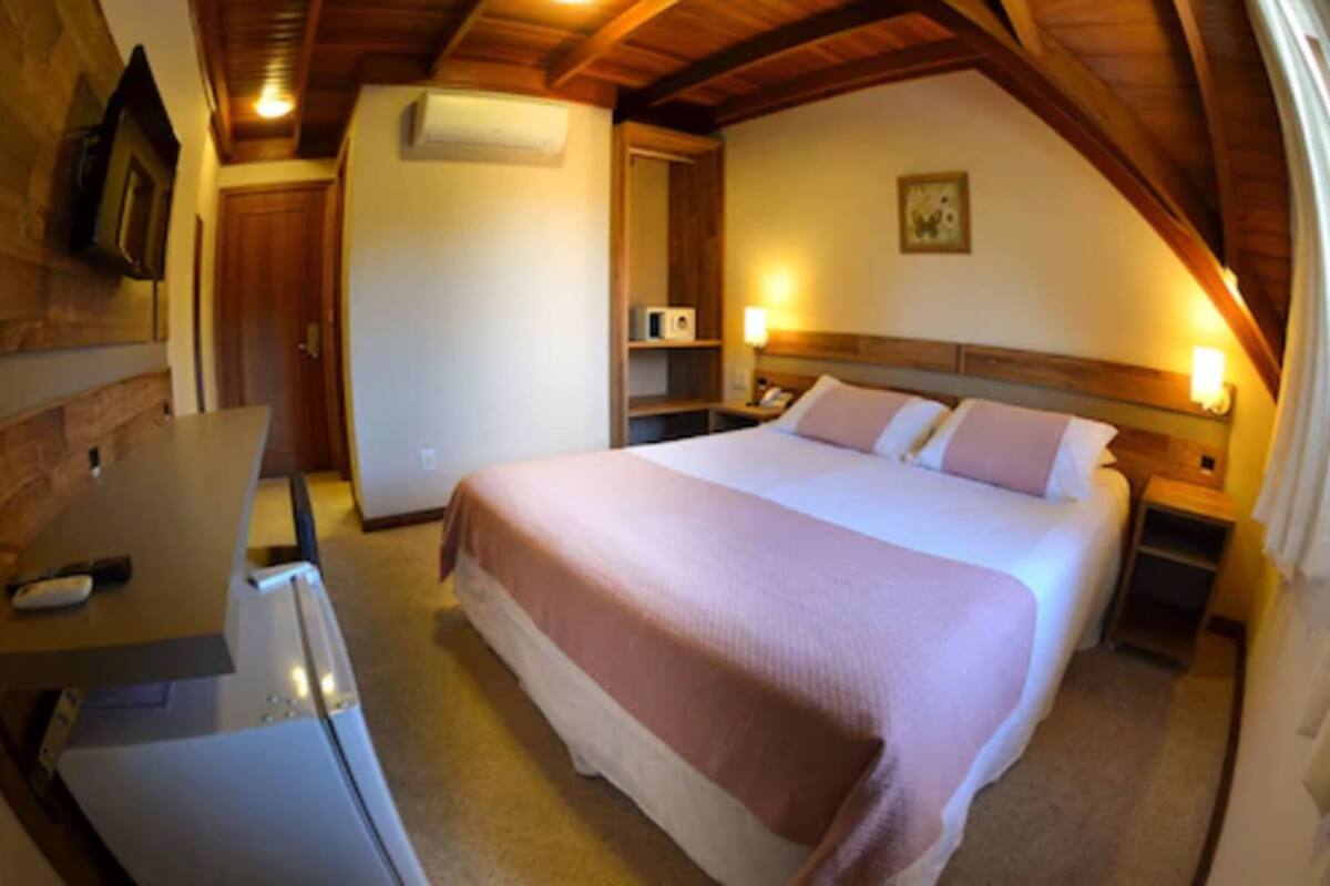 A bedroom with a bed, bedside tables, a desk, and a refrigerator.