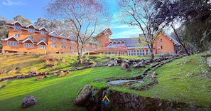 Un hotel con varias construcciones, un paisaje con césped y un arroyo pequeño.