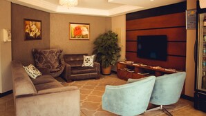 A modern living room with a sofa, armchairs, a coffee table, a TV, and a bookshelf. - Hotel Renascença (Gramado)