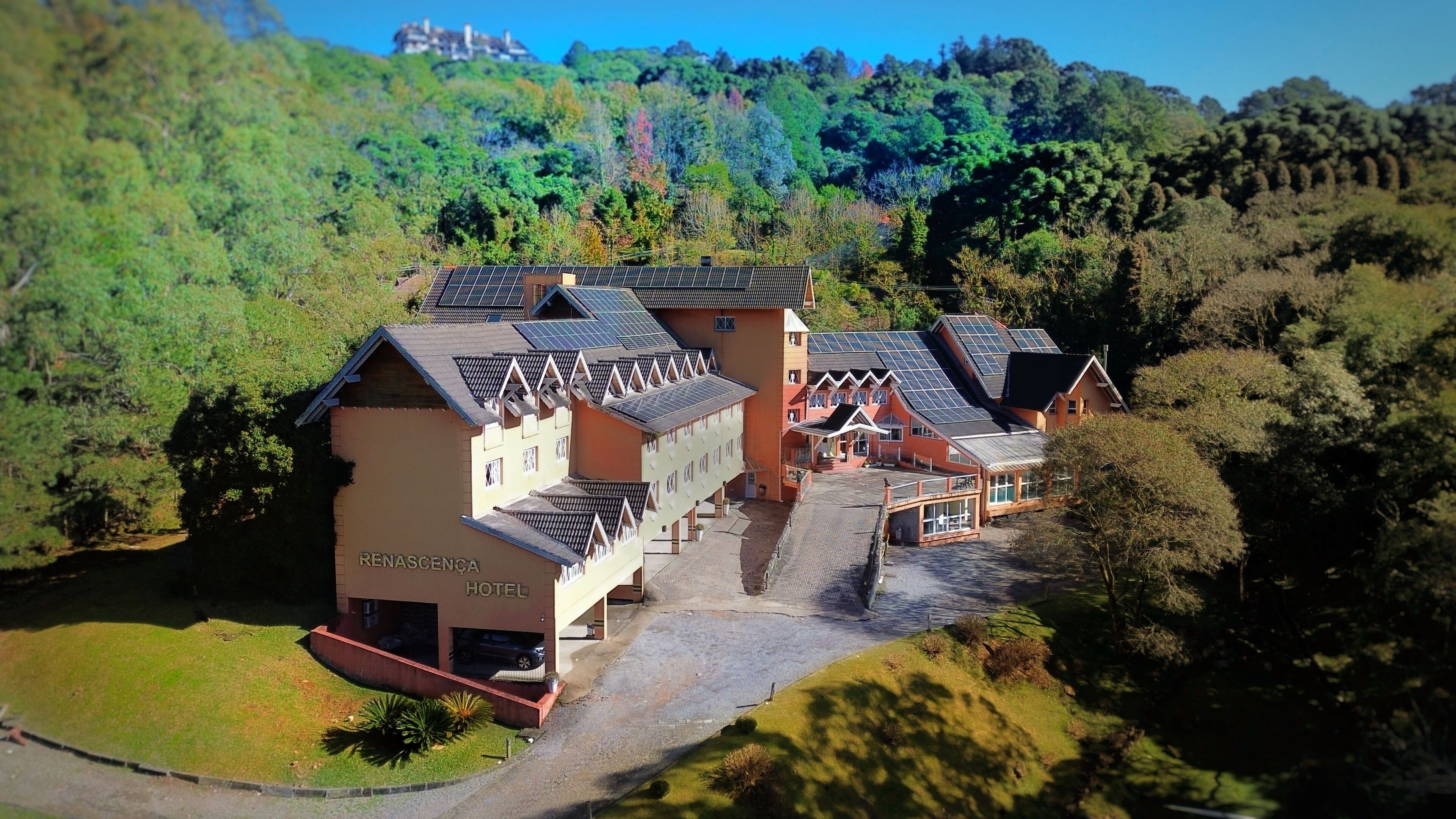 A hotel with multiple buildings, a paved driveway, and a surrounding forested area.