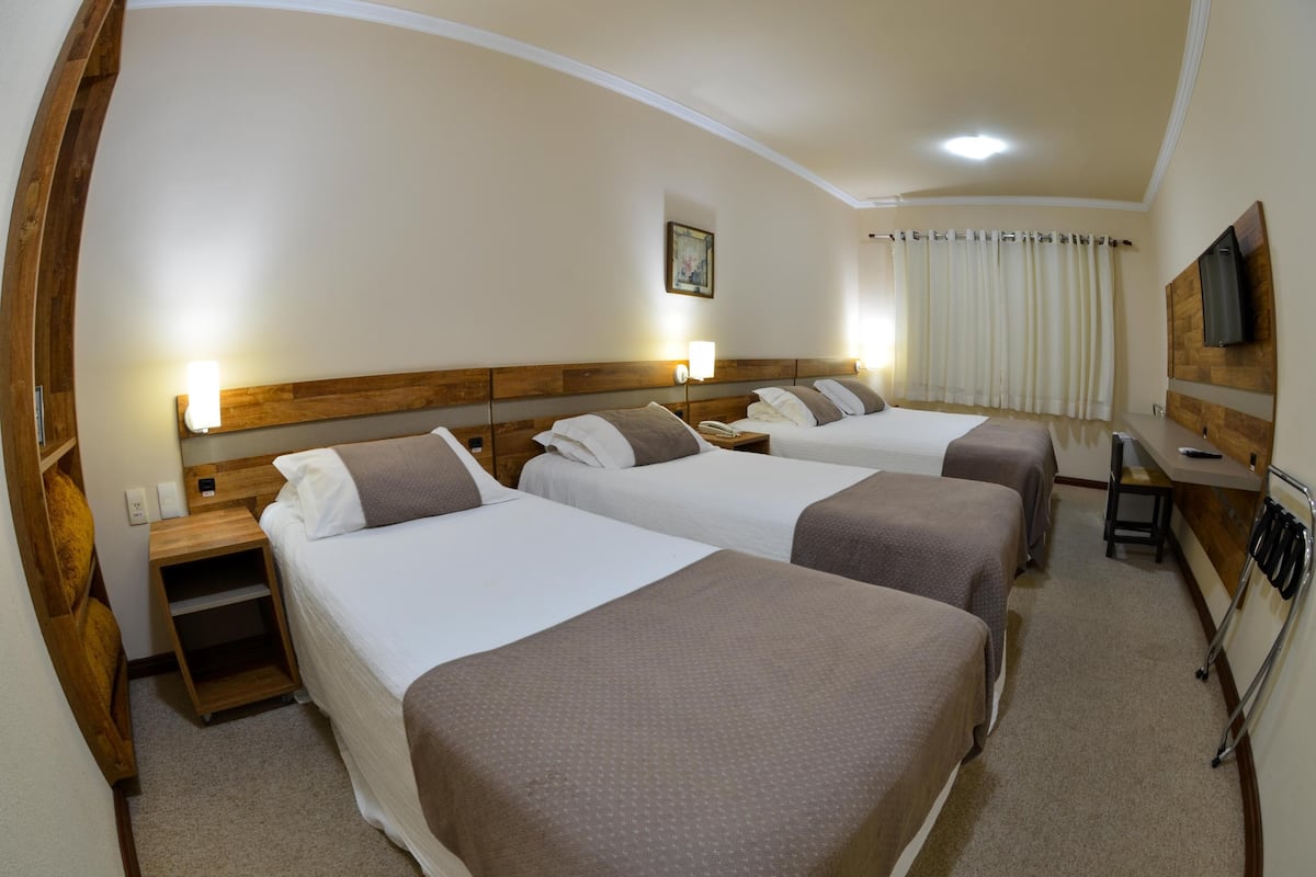 A hotel room with three beds, a desk, a TV, and a painting on the wall.