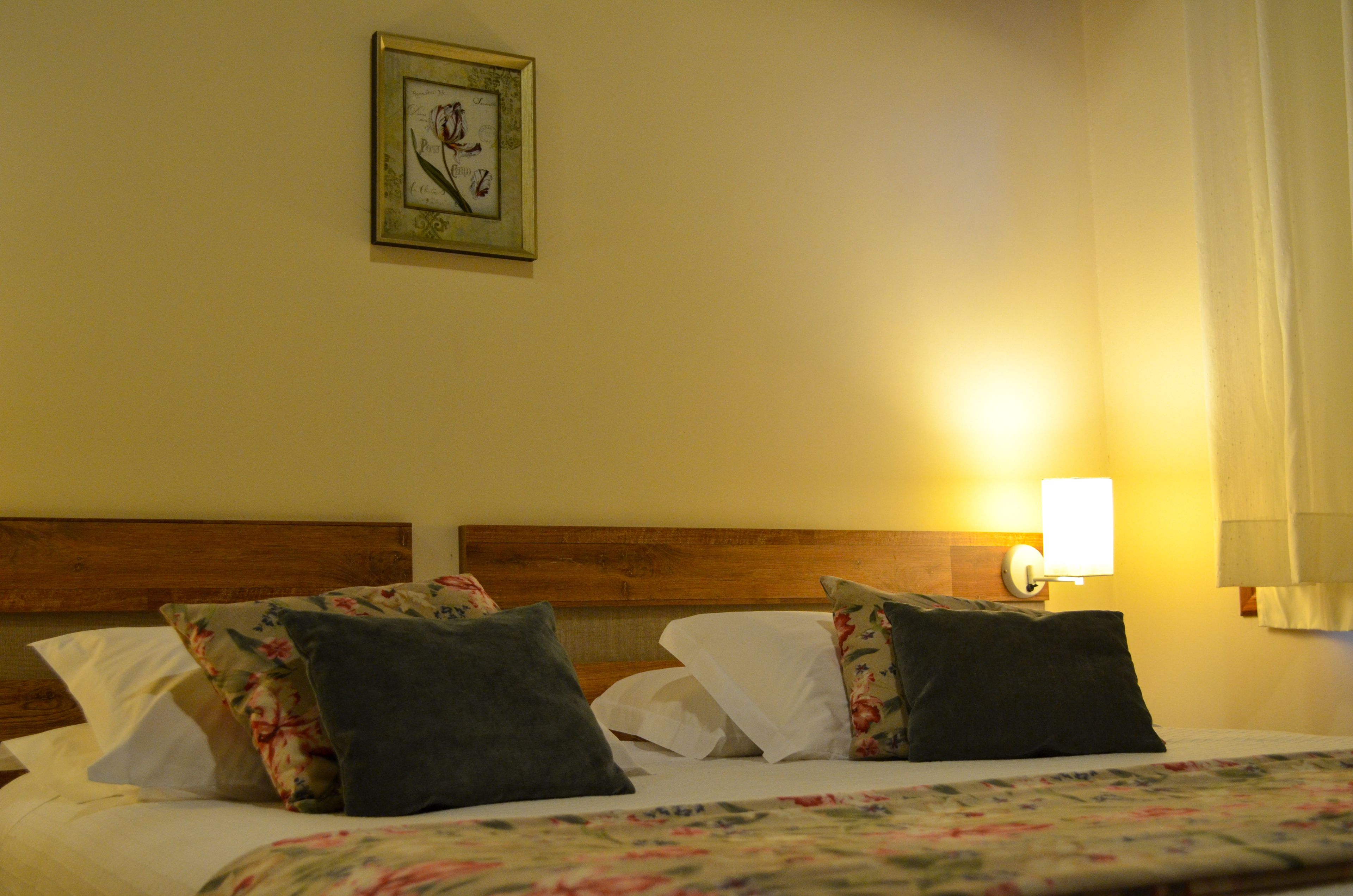 Ein Hotelzimmer mit Holzkopfteil, floralem Bettbezug, einem gerahmten Bild an der Wand und einer Nachttischlampe.