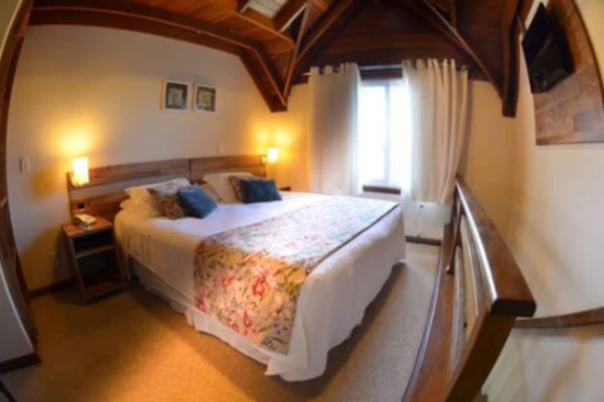 A bedroom with a wooden headboard, a bed with a floral bedspread, two bedside lamps, and a window with curtains.