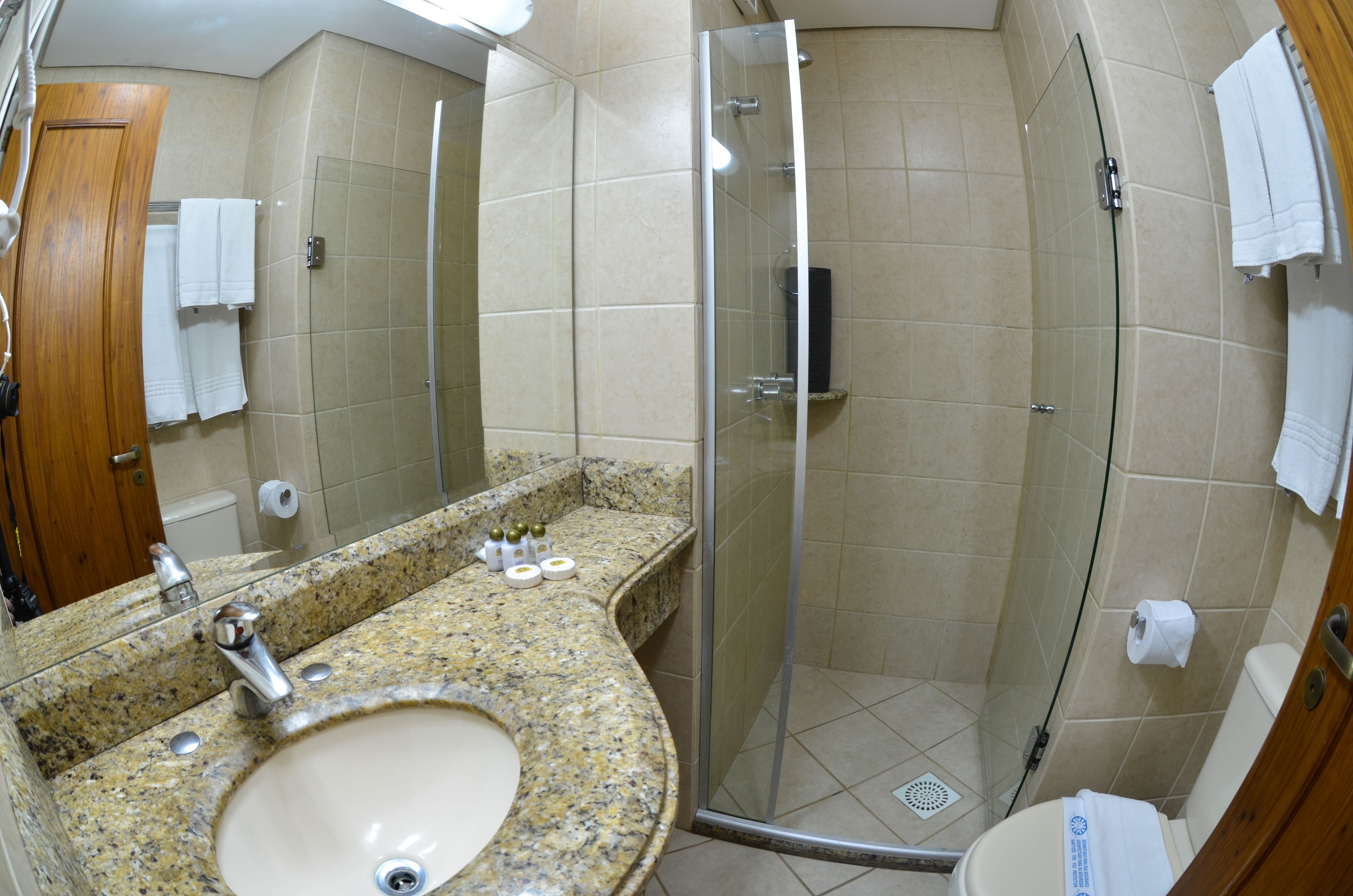 Baño con lavamanos de granito, cabina de ducha de vidrio y paredes con azulejos color beige.