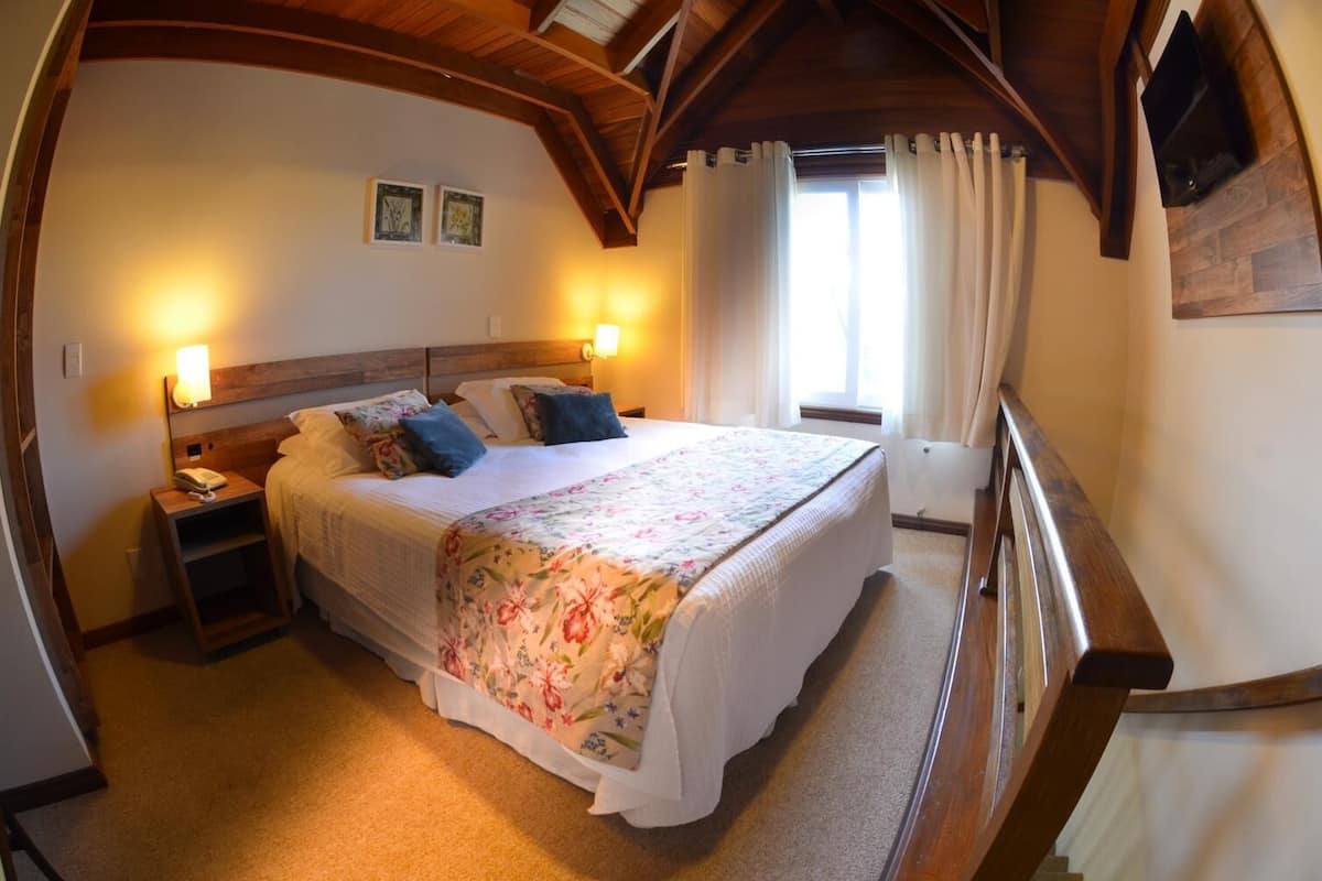 A bedroom with a wooden ceiling, a bed with a floral bedspread, two bedside lamps, and a nightstand with a telephone.