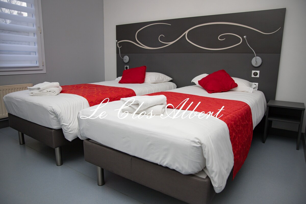 Habitación de hotel con dos camas, cada una con ropa de cama blanca y detalles en rojo, un cabecero moderno y una mesita de noche pequeña.