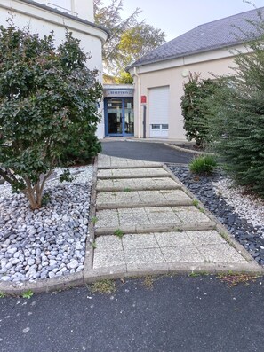 A reception area with a stone pathway leading to a building entrance, surrounded by gravel and small plants. -  LE NID DE LA TOUR (Loudun)