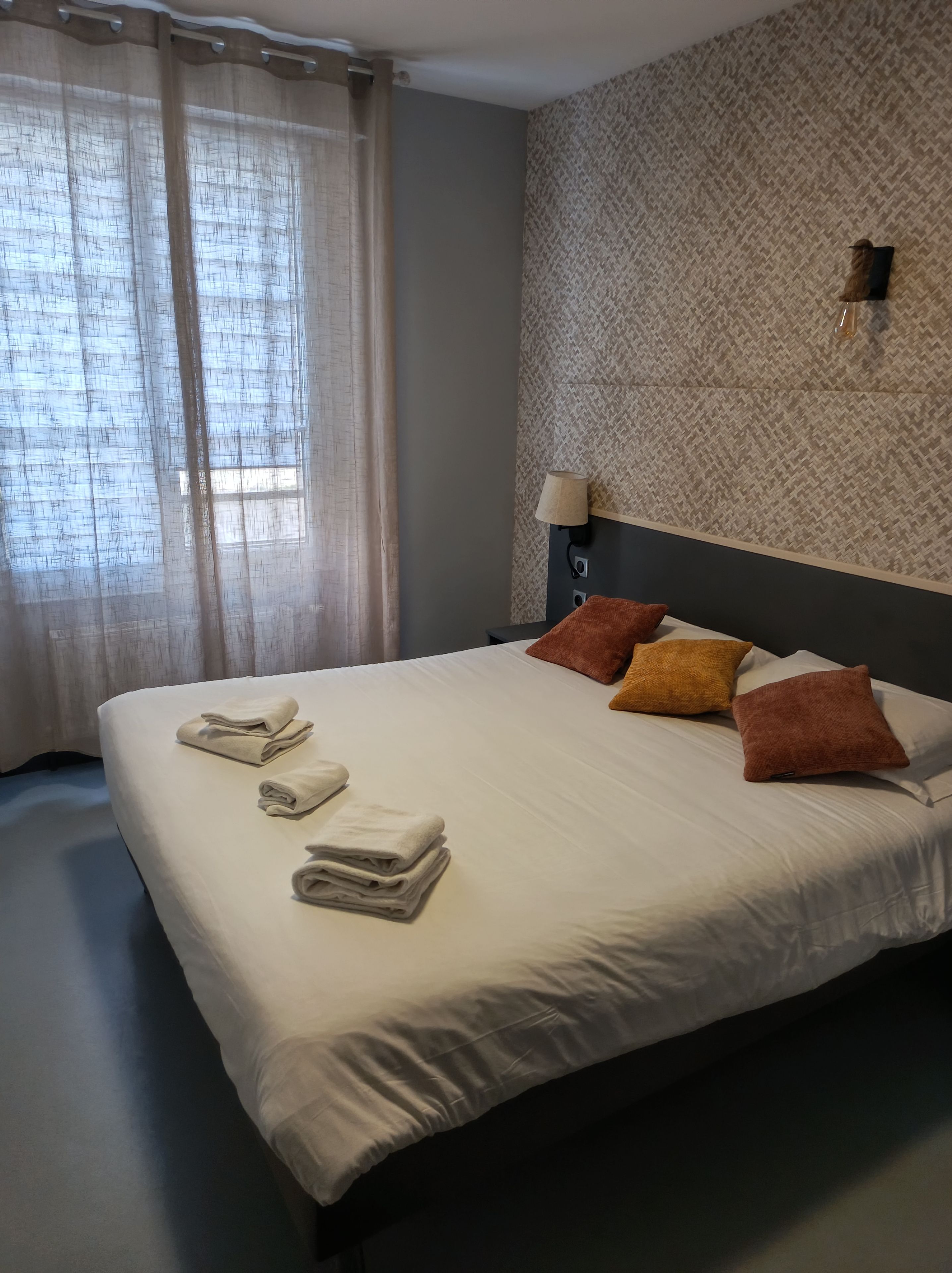 A neatly made bed with folded towels, a patterned wall, and a nightstand with a lamp.