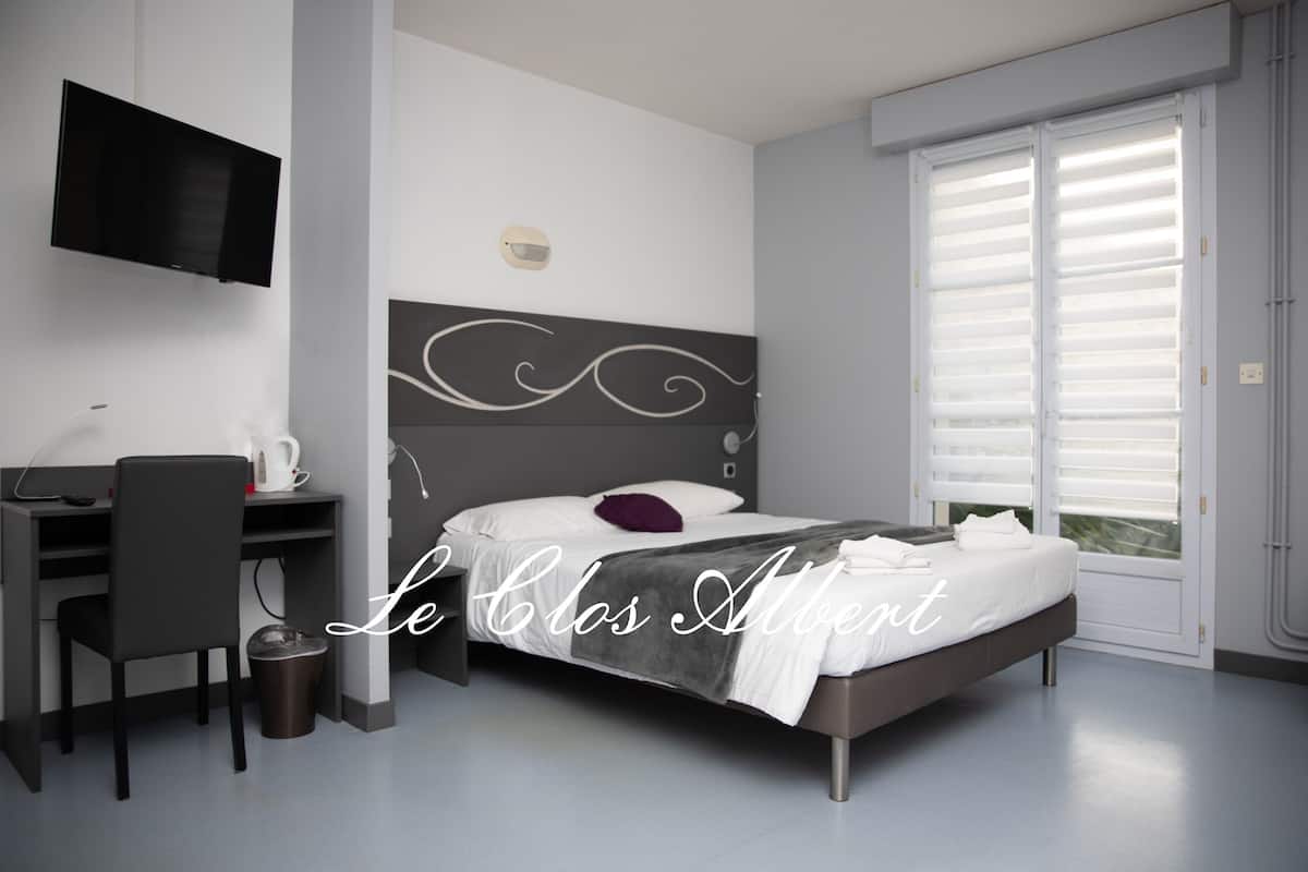 Una habitación de hotel moderna con cama, escritorio, silla, televisor y ventana con persianas.