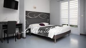 Une chambre d’hôtel moderne équipée d’un lit, d’un bureau, d’une chaise, d’une télévision et d’une fenêtre avec des stores.