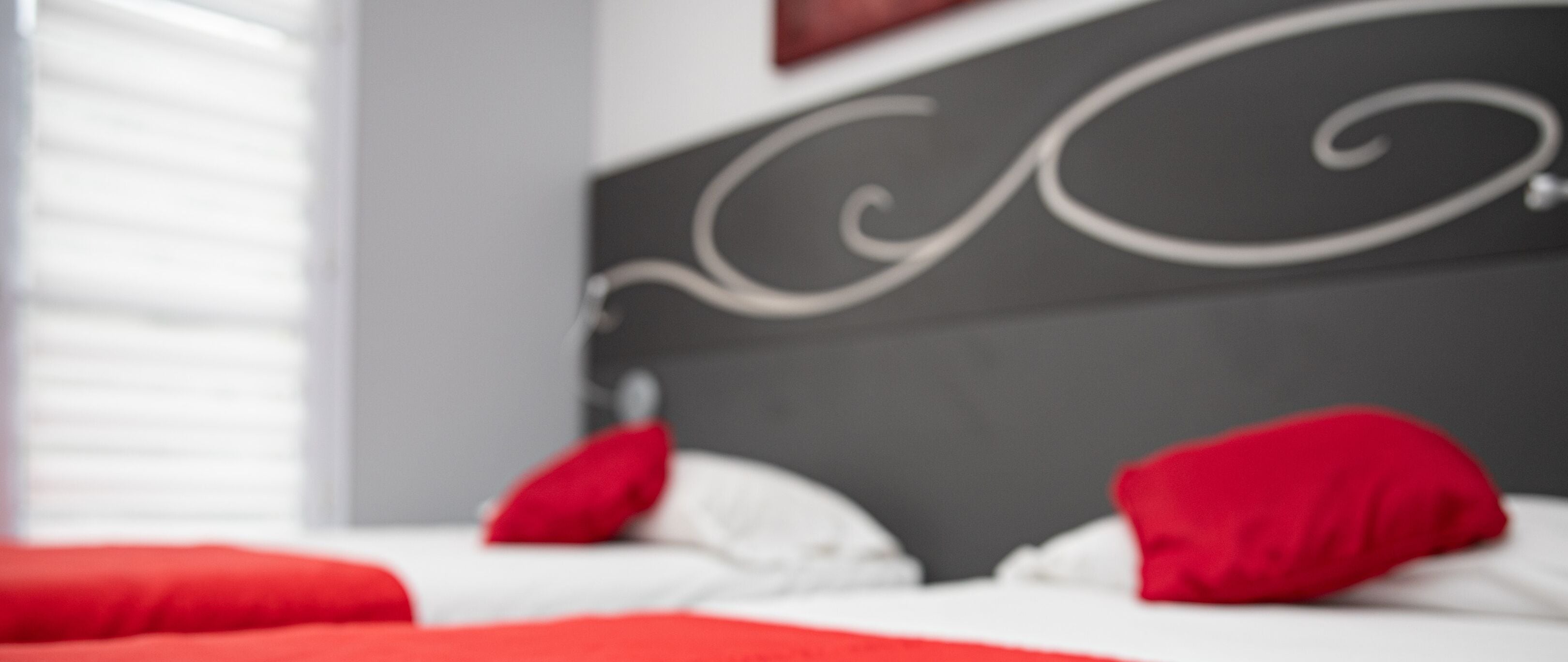 A bed with red pillows and a white bedspread in a room with a grey headboard.