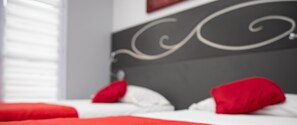 A bed with red pillows and a white bedspread in a room with a grey headboard. -  LE NID DE LA TOUR (Loudun)