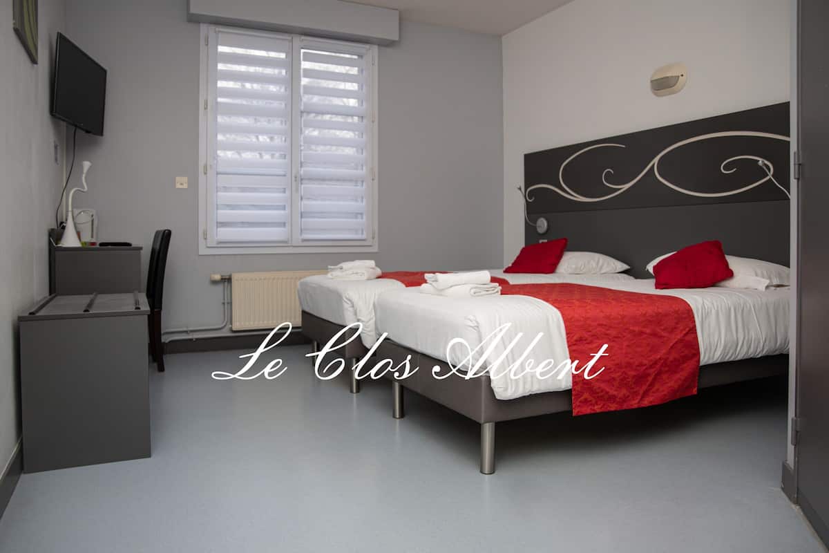 Habitación de hotel con dos camas, un escritorio, una silla, un televisor y una ventana con persianas.