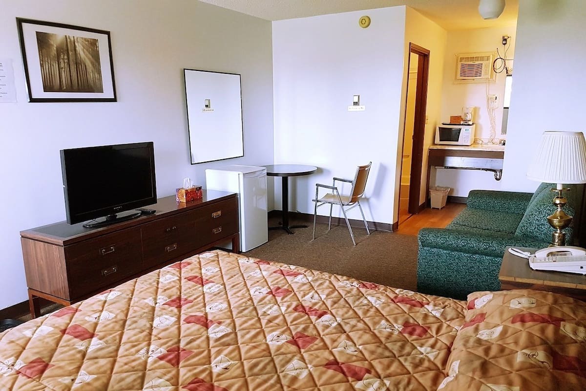 A hotel room with a bed, a television, a desk with a chair, a microwave, and a lamp.