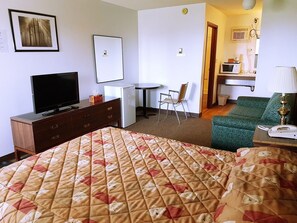 A hotel room with a bed, a television, a desk with a chair, a microwave, and a lamp.