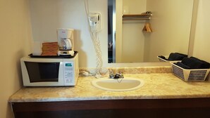 A bathroom with a sink, a mirror, a microwave, and a coffee maker on the countertop. - Elk Point Motel & RV Park (Elk Point)