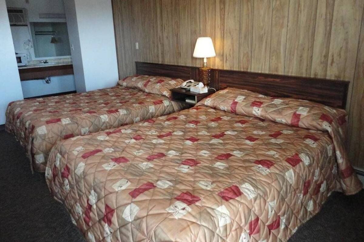 A hotel room with two beds, a wooden headboard, a bedside lamp, and a small table with a telephone.