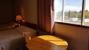 A hotel room with a bed, a table, and a window with a view of a trailer and trees. - Elk Point Motel & RV Park (Elk Point)