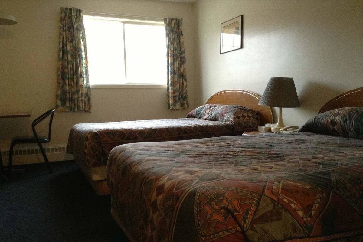 A hotel room with two beds, a chair, a lamp, and a window with curtains.