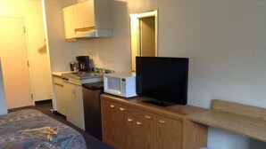 Una habitación de hotel con una cama, un aparador de madera, un televisor, un microondas, una cafetera y un cubo de basura.