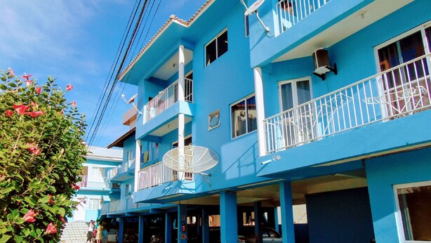 Un edificio de varios pisos con balcones, antenas parabólicas y un área de acceso pavimentada.
