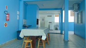 Una habitación con pared azul, una mesa con mantel estampado, taburetes de madera, un lavabo y un extintor.