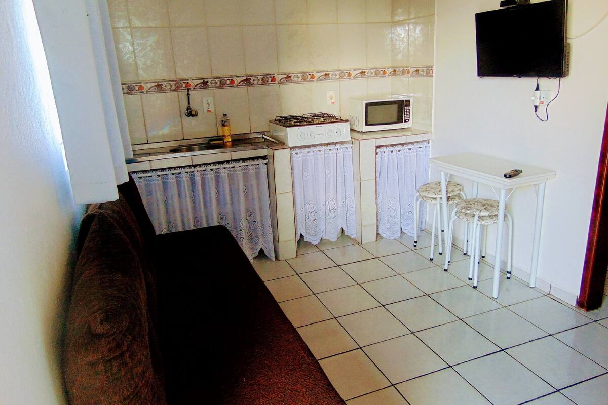 Eine kleine Küche mit einem Gaskochfeld, einer Mikrowelle und einem Tisch mit zwei Stühlen.
