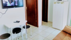 Una sala pequeña con televisor, un mueble blanco, un microondas y un sofá marrón.