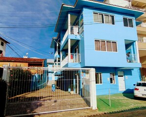 A two-story blue building with balconies, a gated entrance, and a parked car.