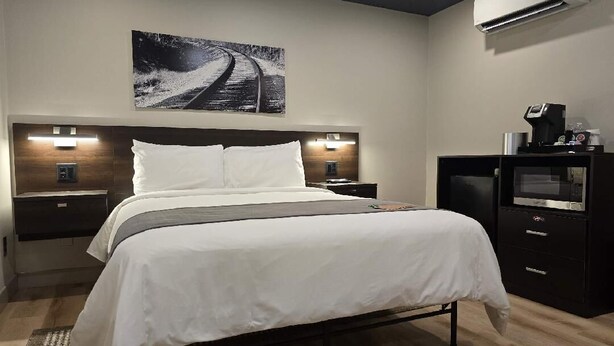 A modern hotel room with a large bed, bedside lamps, a flat-screen TV, and a wall-mounted air conditioner. - Sugarcreek Village Inn (Sugarcreek)
