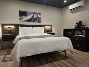 A modern hotel room with a large bed, bedside lamps, a flat-screen TV, and a wall-mounted air conditioner. - Sugarcreek Village Inn (Sugarcreek)