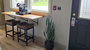 A room with a desk, two chairs, a potted plant, a door with a doormat, and a window with blinds. - Sugarcreek Village Inn (Sugarcreek)