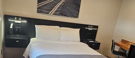 Een keurig opgemaakt bed met witte lakens, een hoofdbord, nachtkastjes, een bureau en een stoel.
