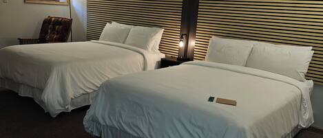 Ein Hotelzimmer mit zwei Betten, einem Sessel, einem Nachttisch, einer Lampe und einem Spiegel.