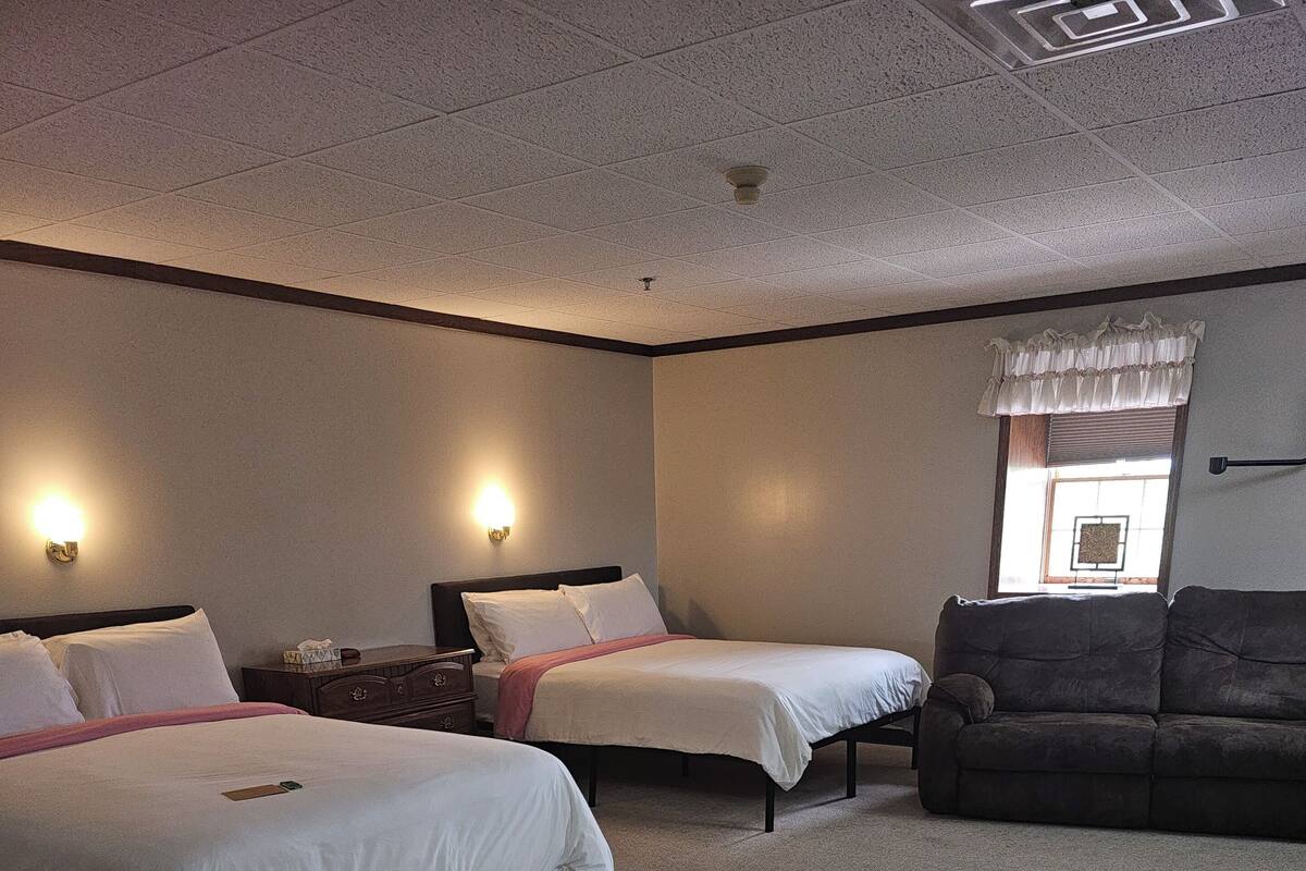Una habitación de hotel con dos camas, un sofá, una mesita de noche y una ventana con persianas.
